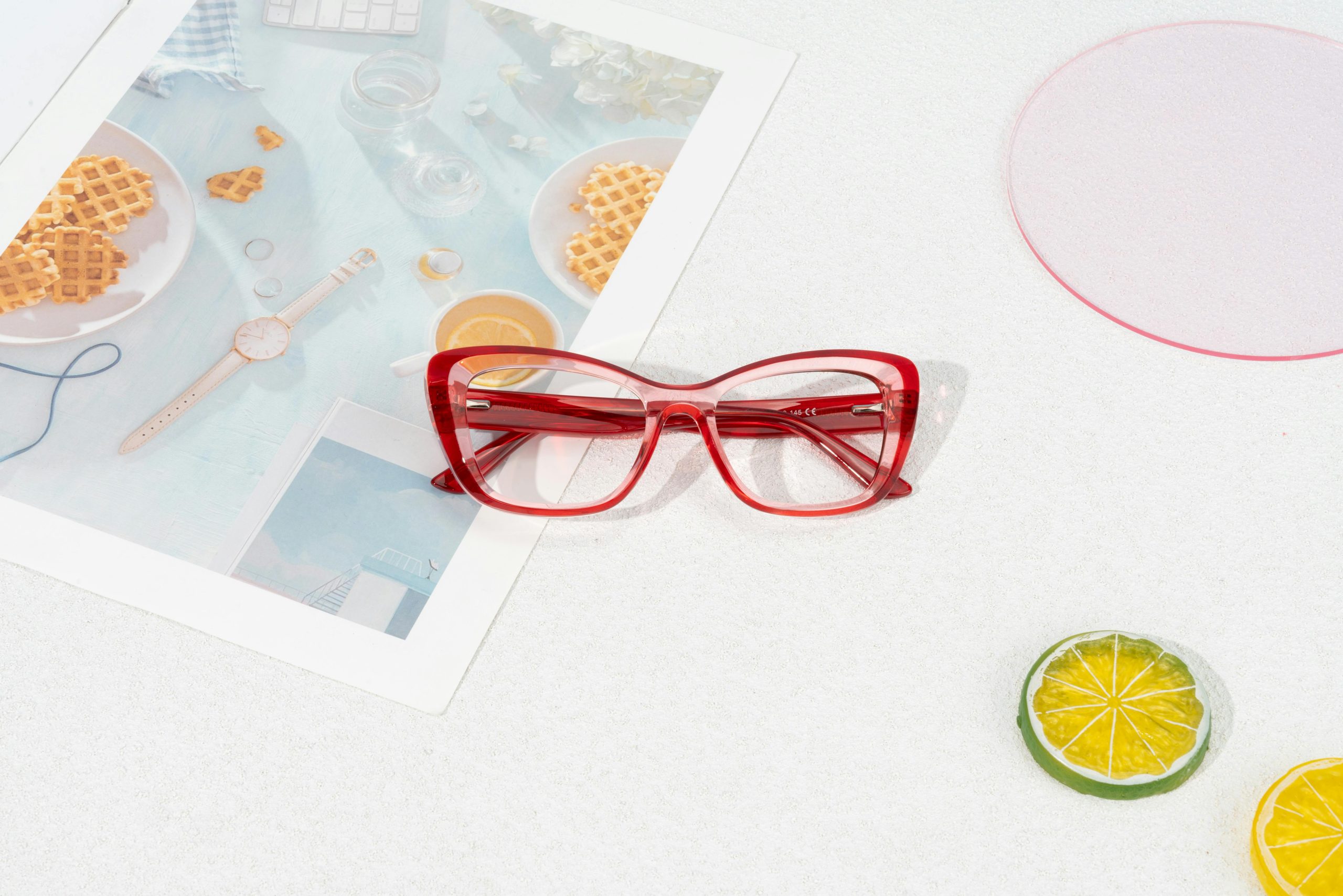 Red glasses on a magazine with citrus slices, creating a vibrant, stylish vibe.