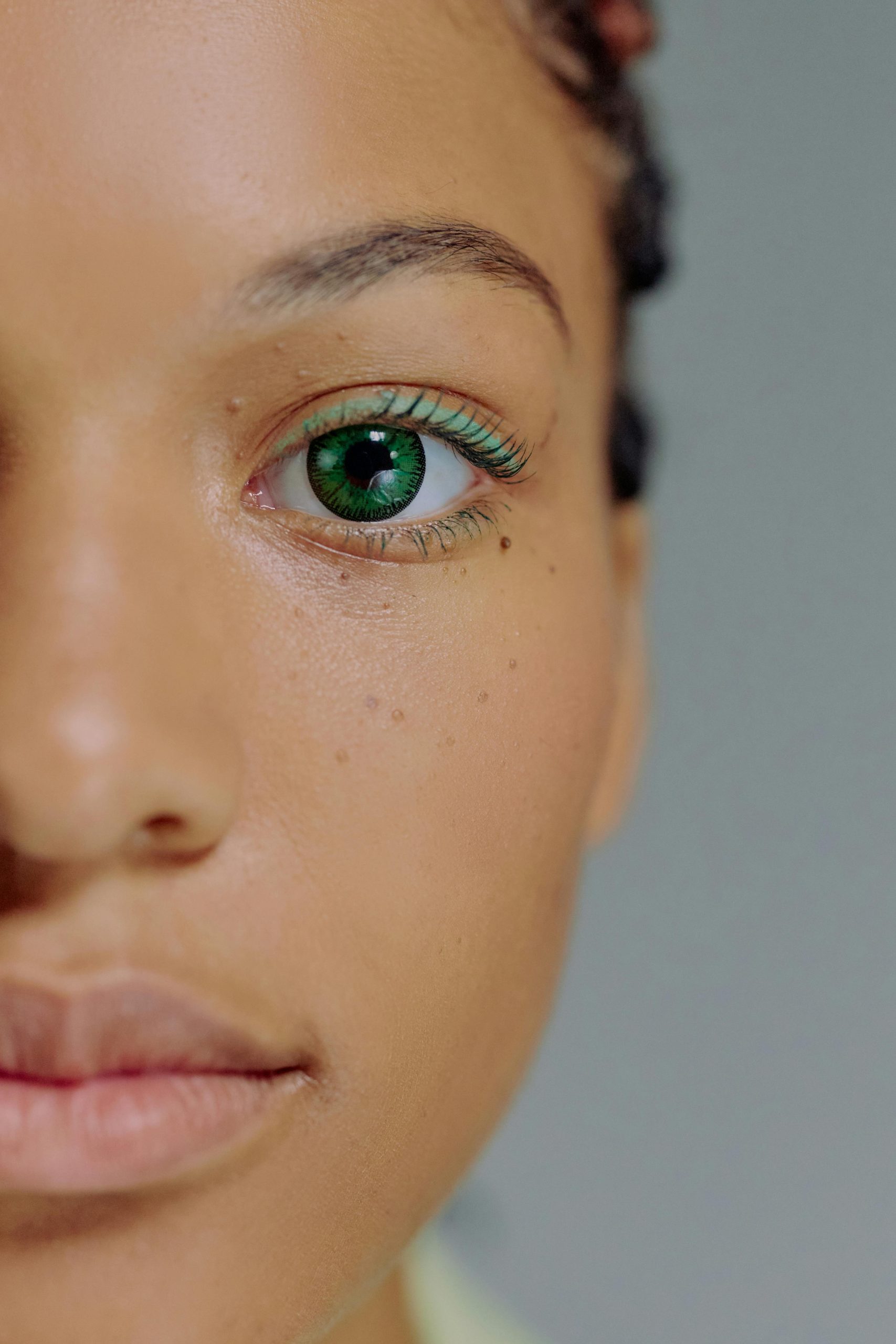 Intimate close-up of a woman's face highlighting green eyes and natural makeup.